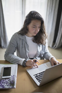 Young woman using phone while sitting on table