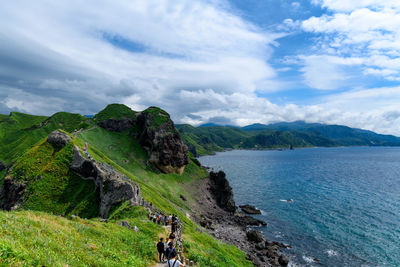 People hiking on mountain by sea against sky