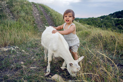 Baby boy playing in the field with a small goat