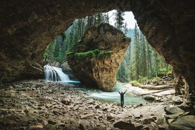 Rear view of mid adult man with arms raised standing in forest seen through cave