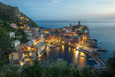 High angle view of illuminated buildings by sea against sky