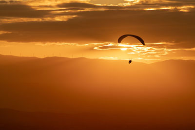 Silhouette person paragliding against sky during sunset