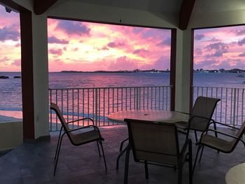 Empty chairs and table by sea against sky during sunset