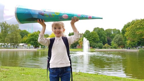 Full length portrait of smiling boy standing on lake against trees