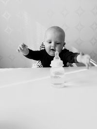 Curious bay boy looking at milk bottle at table against wall