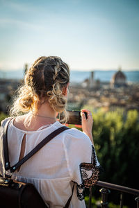 Rear view of woman looking at cityscape against sky