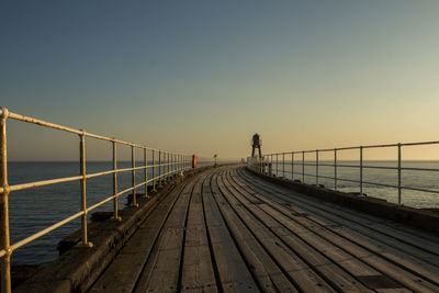 Pier over sea against clear sky during sunset