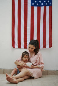 A young woman sitting with her daughter with the american flag in the background.