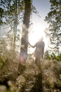 Woman standing by tree in forest against sky