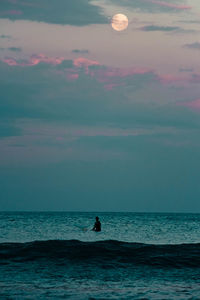 Silhouette man in sea against sky during sunset