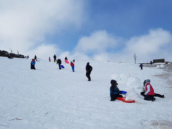 People enjoying on snow covered field against sky