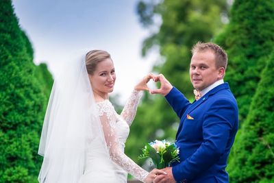 Portrait of bride and groom making heart shape with hands