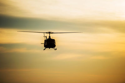 Low angle view of silhouette helicopter flying in sky during sunset