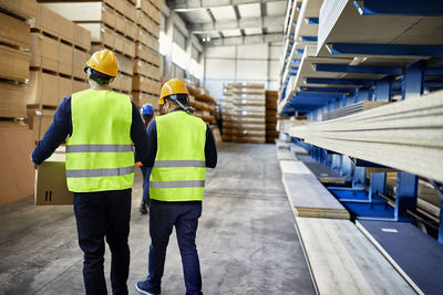 Rear view of two workers carrying boxes in factory warehouse