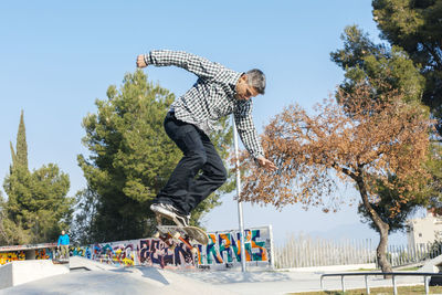 Low angle view of man jumping by trees against sky