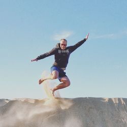 Low angle view of playful man jumping on sand dune against sky