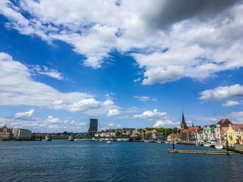 View of buildings by river against cloudy sky