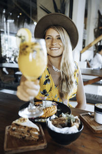 Smiling young woman holding drink at table in restaurant