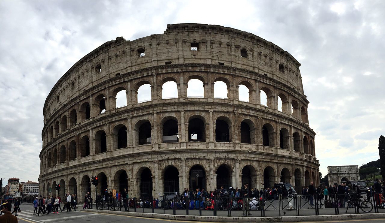 travel destinations, travel, tourism, history, architecture, cultures, built structure, tourist, large group of people, sky, cloud - sky, old ruin, the past, ancient, building exterior, low angle view, amphitheater, outdoors, day, vacations, city, group of people