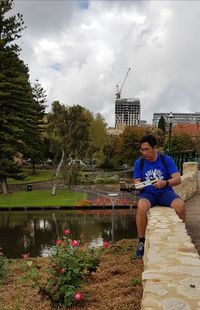 Young woman sitting on grass in park against sky
