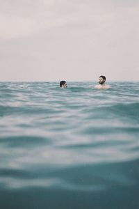Men swimming in sea against sky