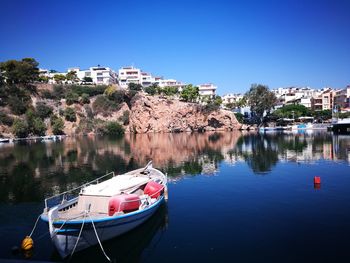 Sailboats moored in city by buildings against clear blue sky