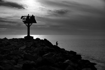 Silhouette rocks on beach against sky during sunset