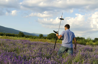 Rear view of surveyor using equipment on lavender field against cloudy sky