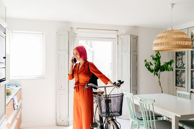 Portrait of young woman with bicycle standing against wall at home