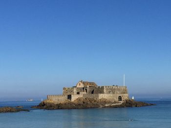 Castle by sea against clear blue sky