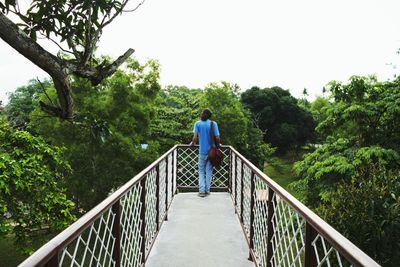 Rear view of man standing on footbridge against clear sky
