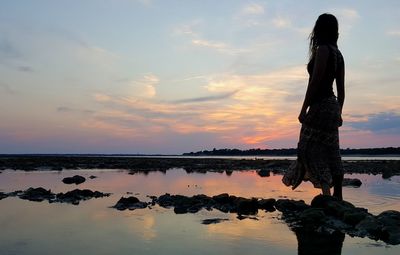 Woman standing by sea against sky during sunset