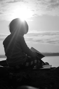 Rear view of man sitting on lake against sky