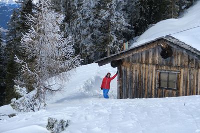 Mature woman standing by log cabin on snowcapped mountain