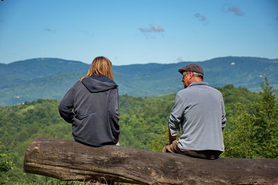 Senior couple sitting on tree trunk and looking over hills