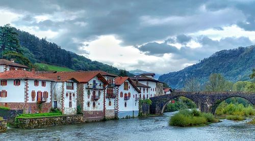 Arch bridge over river amidst buildings against sky