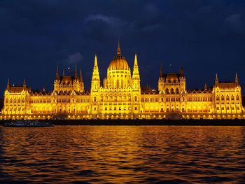 Illuminated hungarian parliament building by danube river against sky at night