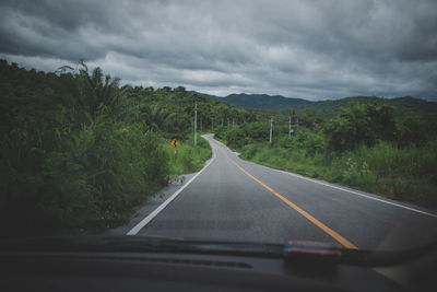 Empty road against cloudy sky seen through car windshield