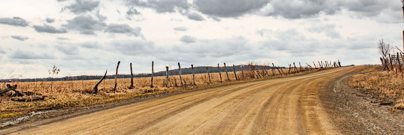 Panoramic view of dirt road on field against sky