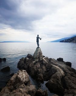 Man standing on rock by sea against sky