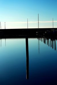 Wooden posts in lake against clear blue sky