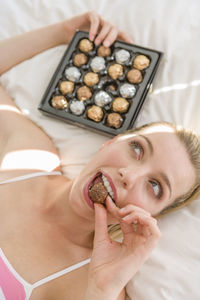 High angle view of thoughtful woman eating chocolate while lying on bed