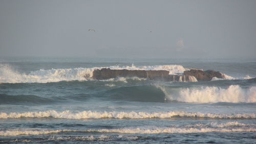 Waves breaking on rock against clear sky