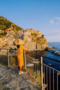 Rear view of woman standing on railing by sea against sky