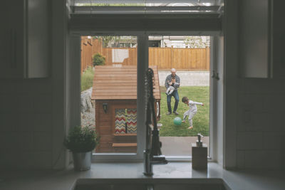 Father and sons playing in lawn seen through window at home