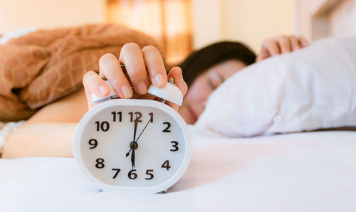 Close-up of woman holding alarm clock while lying on bed at home