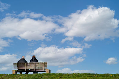 Men sitting on bench on field against sky
