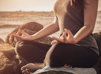 Low section of woman meditating on rock at beach