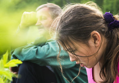 Side view of sad granddaughter sitting with grandfather at field