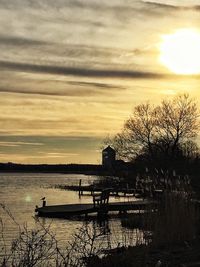 Silhouette trees by lake against sky during sunset